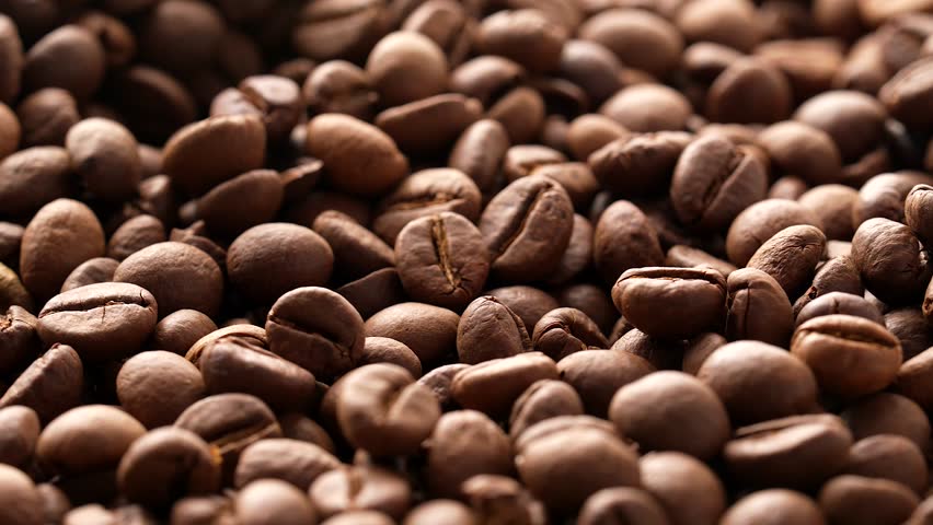 A closeup shot of a pile of coffee beans rotating under bright natural light, with blurred background