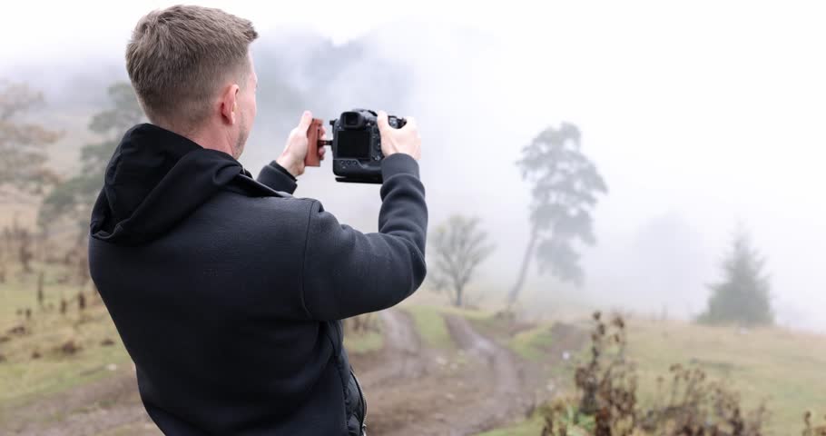 Man photographer captures stunning image of vast field covered with thick layer of morning fog. Male adjusts settings on professional camera