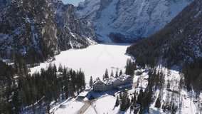Aerial view of Braies Lake in northern Italy during winter, with a frozen surface, snow covered cliffs, evergreen forests, and scattered figures. - Powered by Shutterstock - Get 15% off with code: PIKWIZARD15