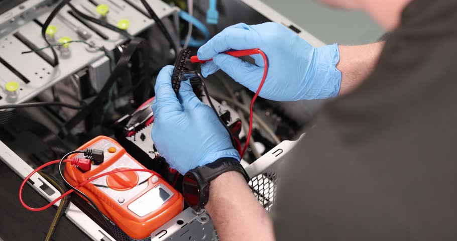 Man in rubber gloves solders contacts with soldering iron. Complex mechanism with several colorful wires needs repair from professional mechanic
