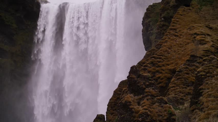 Powerful waterfall flowing between mossy cliffs in Iceland