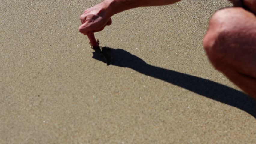 Hand drawing heart on the sand, sandy beach in a sunny afternoon. Heart drawn in the sand at a beautiful beach during a sunny holiday on the coast, man's hand