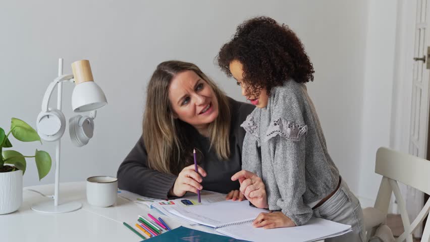 Caucasian mother and African American daughter studying at home, doing homework in cosy white room. Parent teach, child school girl learn knowledge, write exercise read book. Education for children
