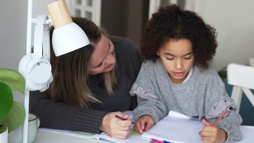 Caucasian mother and African American daughter studying at home, doing homework in cosy white room. Parent teach, child school girl learn knowledge, write exercise read book. Education for children