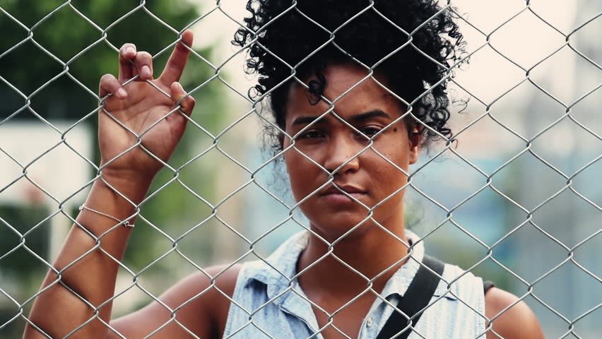 Lonely Young African American woman standing behind metal fence barrier feeling sad and solitude, mental illness concept