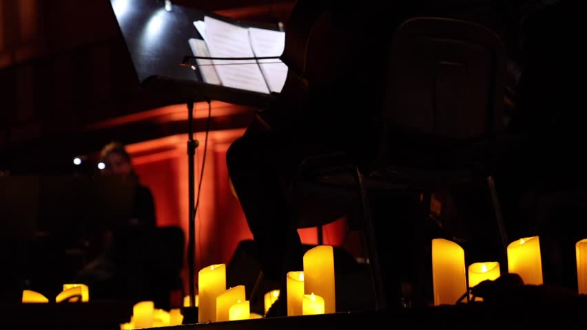 Musicians of an orchestra or ensemble performing surrounded by numerous lit candles. 