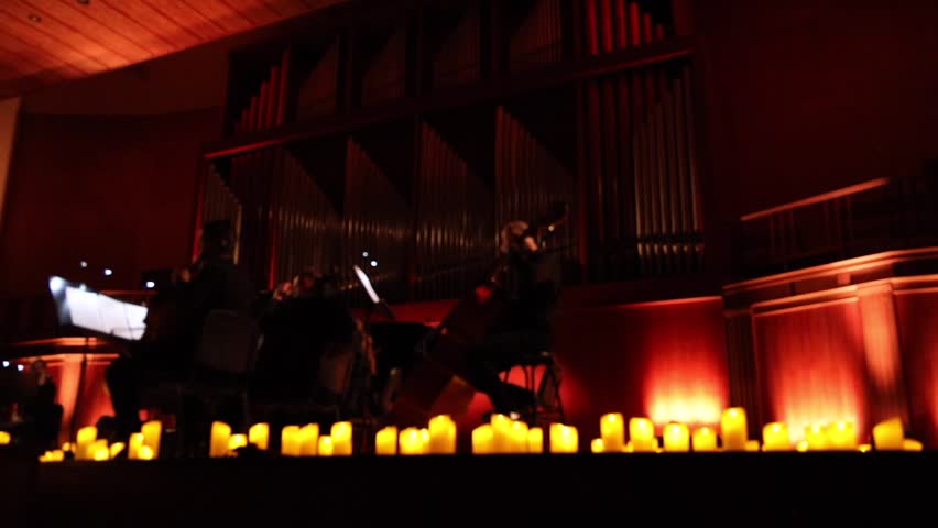 Musicians of an orchestra or ensemble performing surrounded by numerous lit candles. Bokeh, blurred background.
