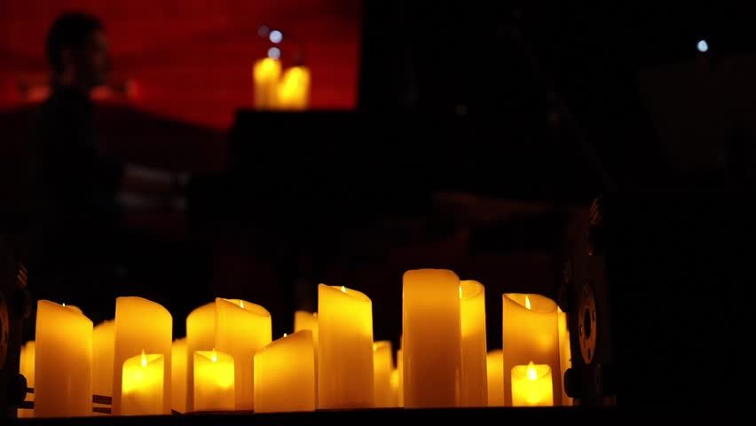 Musicians of an orchestra or ensemble performing surrounded by numerous lit candles. 