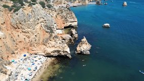 A vertical drone video showcases Marinha Beach in Portugal, highlighting a sea-surrounded cliff with a central hole, creating a striking natural arch formation.  A boat navigates inside the cliff - Powered by Shutterstock - Get 15% off with code: PIKWIZARD15