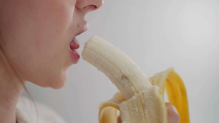 close up of lady savoring banana in bright environment with natural light highlighting details of fruit texture and hand grip while enjoying healthy snack during relaxed calm indoor moment