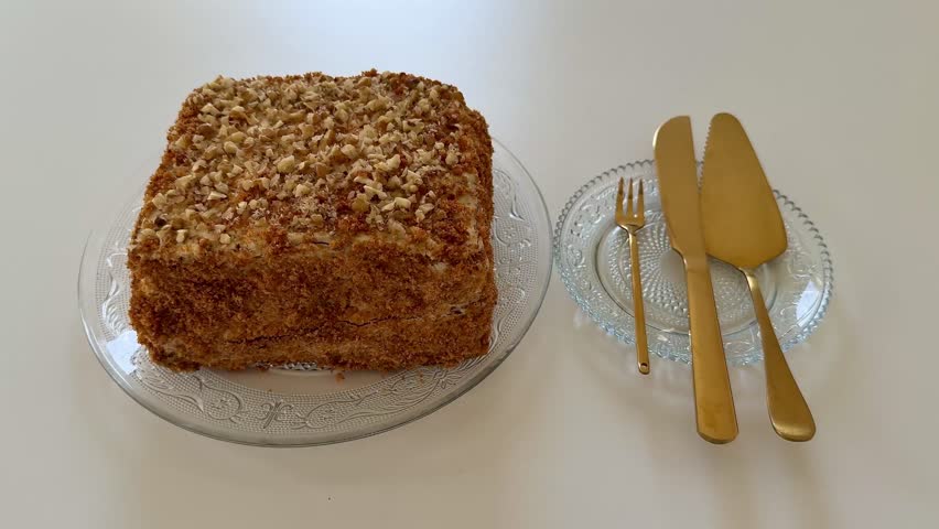 An exquisitely presented square cake, delicately topped with an assortment of nuts, on a vintage glass platter