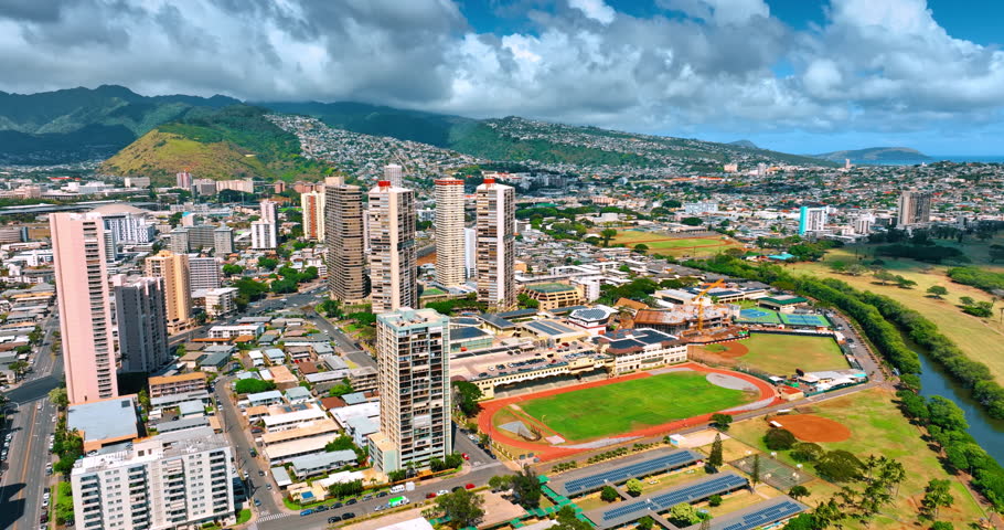 Spectacular view of Honolulu, Hawaii, USA at the backdrop of green mountains. Fluffy cloudscape covers the sky. Aerial perspective.
