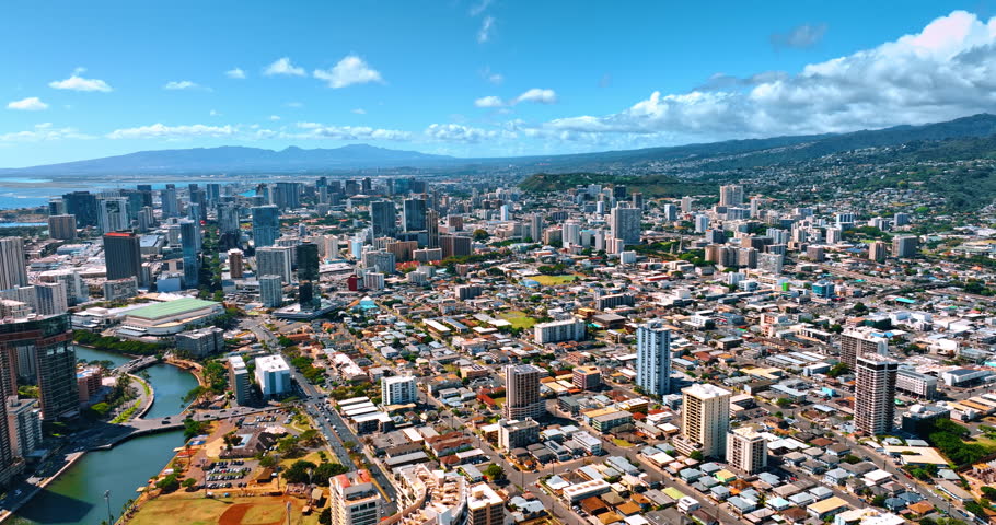 Sunny vast cityscape stretching to the slopes of mountains. Fluffy clouds over the city panorama. Aerial view. Honolulu, Hawaii, USA.