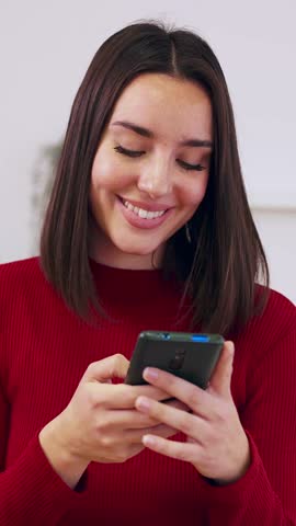 Vertical HD video of smiling woman relaxing at home using cell phone device. Beautiful millennial female chatting on mobile phone application. Social media and technology concept.
