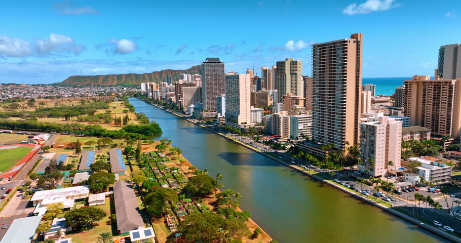 Flying above the Ala Wai Canal along the length of Waikiki. Sunny view of Honolulu, Hawaii, USA with Koko Head Crater at backdrop.