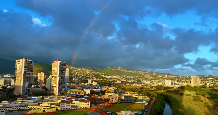 Enormous clouds gathered above the scenery of Honolulu at sunset. Beautiful bright rainbow raises over the city. Hawaii, USA.