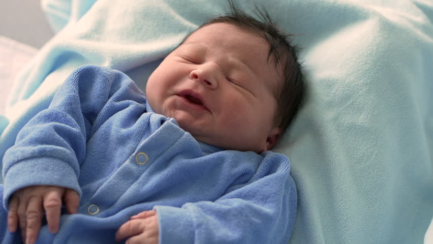 Peaceful newborn baby resting in a blue onesie, lying in a hospital bed, with soft lighting highlighting the baby's delicate features and tiny hands, showcasing newborn care