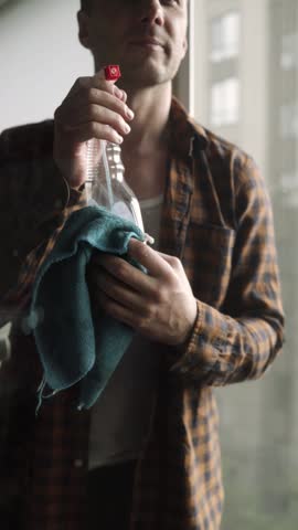 Close Up Man Hands Cleaning a Window Using Sprayed Liquid.