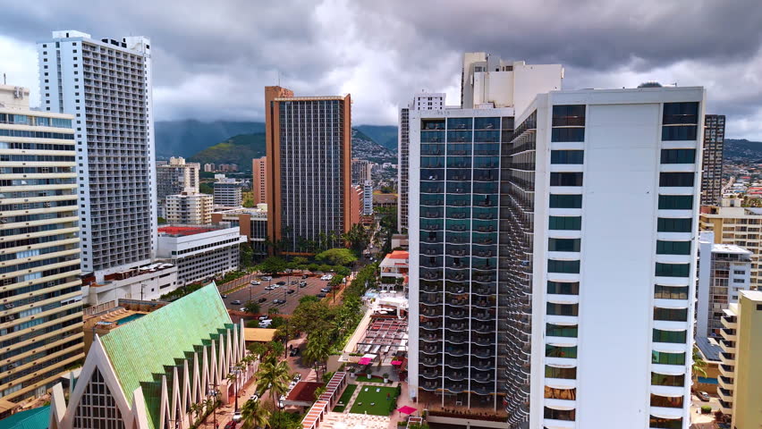 Approaching a parking lot situated among the high-rise buildings. Drone footage in Honolulu, Hawaii, USA. Dramatic cloudscape at backdrop.