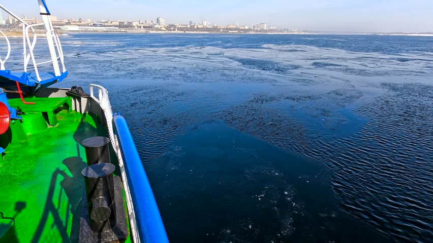 View of a boat moving along the water surface of a cold winter river, breaking the thin ice and creating small white waves on the side.