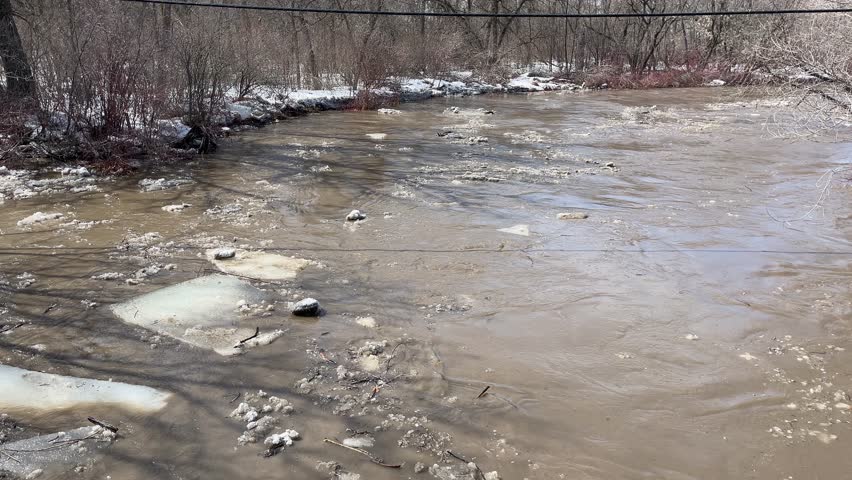 Fast flowing muddy spring river full of pieces of ice flooding as the ice blocks tumble