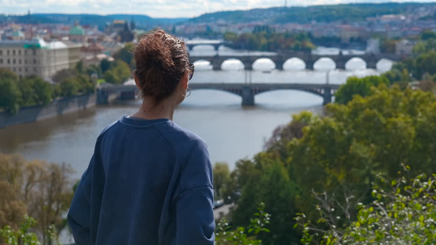 Tourist admiring river and bridges in prague. Young woman wearing sunglasses standing at scenic viewpoint overlooking panoramic view of vltava river and historic bridges in prague during sunny day
