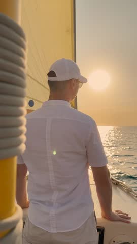 Sail for dream. Yacht captain in white shirt travel on ocean. Man traveling on ocean on yacht watching sunrise. Young man sailing on yacht under white sail. Sea travel. Ship sailing sea man looks sun