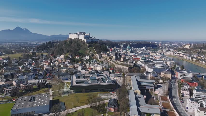 Sweeping aerial view of Salzburg, Austria, showcasing the Salzach River, Hohensalzburg Fortress, historic architecture, and surrounding hills.