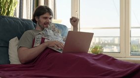 Freelancer man making money online using laptop, lying on bed in the morning, earn money from the comfort of bed. Cash flow. Money rain flow through the laptop. Dollar bills flying in investor face - Powered by Shutterstock - Get 15% off with code: PIKWIZARD15