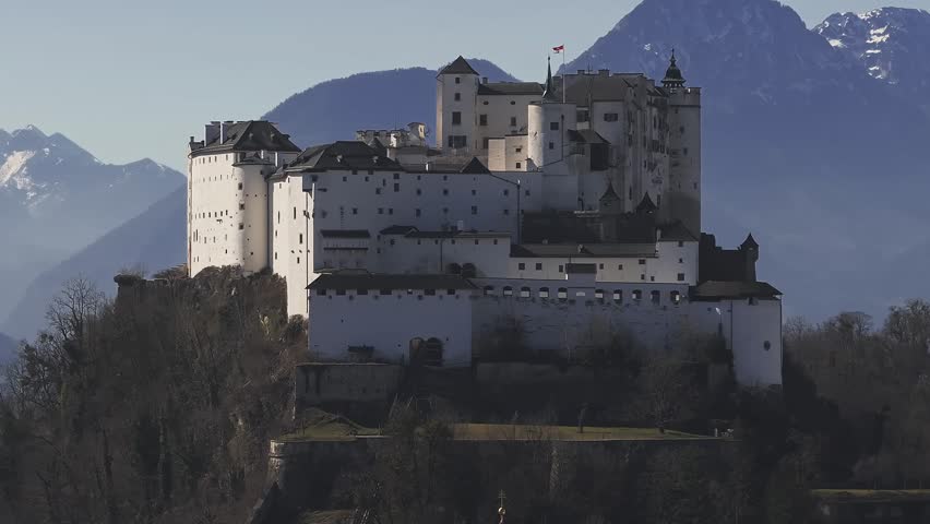 Aerial view of Hohensalzburg Fortress in Salzburg, Austria, with the Alps in the background. The camera moves smoothly, capturing winter scenery.