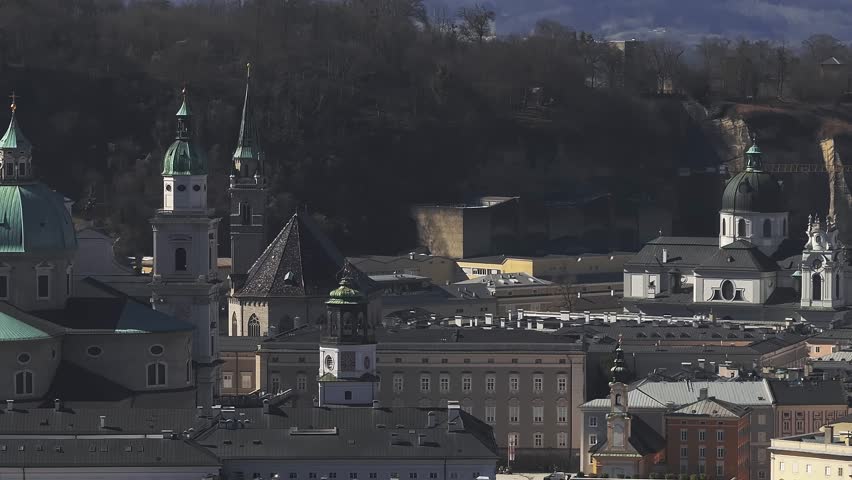 Aerial view of Salzburg, Austria, featuring the Salzburg Cathedral, Hohensalzburg Fortress, colorful facades, and wooded hills on a clear day.