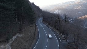 White car travels a winding mountain road through a forested valley with snowy hills in the distance - Powered by Shutterstock - Get 15% off with code: PIKWIZARD15