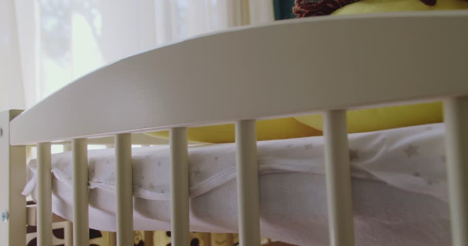 Wooden crib with protection borders in nursery room. Modern baby bed with soft toy and bedding. Closeup of soft toy lying in baby bed in nursery room. Preparing room for newborn.