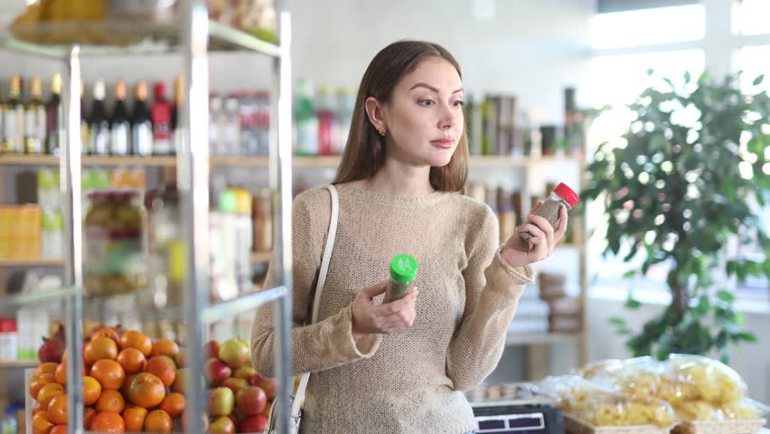Young woman buyer chooses spices and seasonings in jar in grocery store