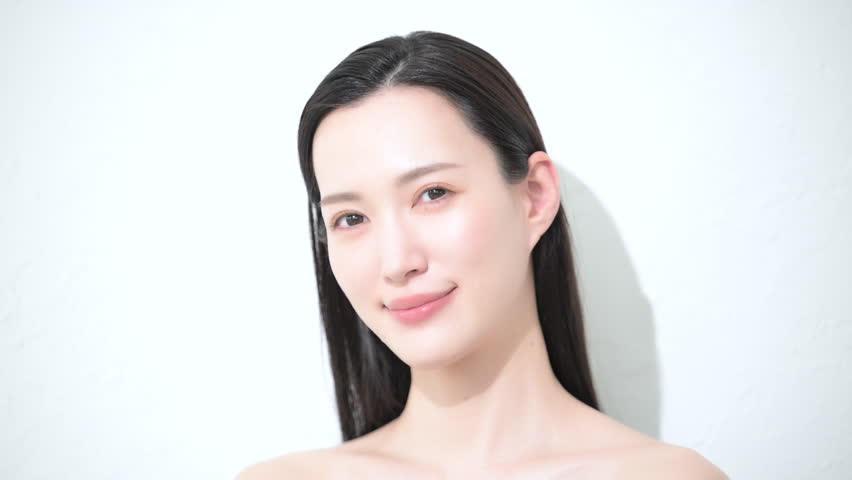 video of a frontal beauty image of a young woman with beautiful dark hair, glossy and bare skin, looking at the camera close-up.	