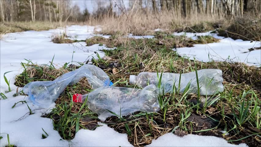 There is garbage in the forest in the form of empty plastic bottles after winter, in spring. slow-motion fall of an empty plastic bottle onto the green grass. Plastic bottles are like garbage in the s