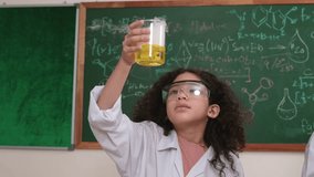Attractive american student hold beaker and inspect biochemical solution. Close up of curious girl stirring beaker and looking at color changing while standing at laboratory with blackboard. Pedagogy. - Powered by Shutterstock - Get 15% off with code: PIKWIZARD15