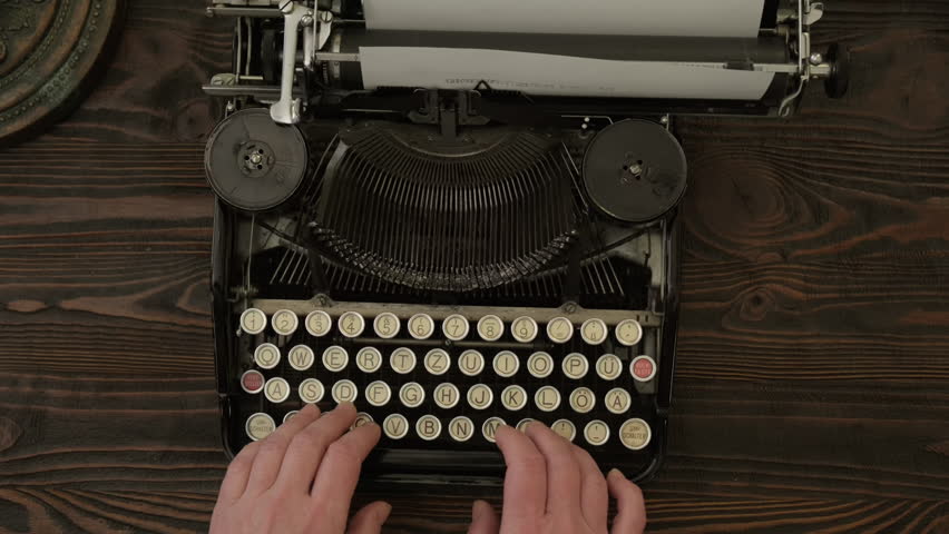 Man hands typing on old vintage typewriter on wooden desk top view close up