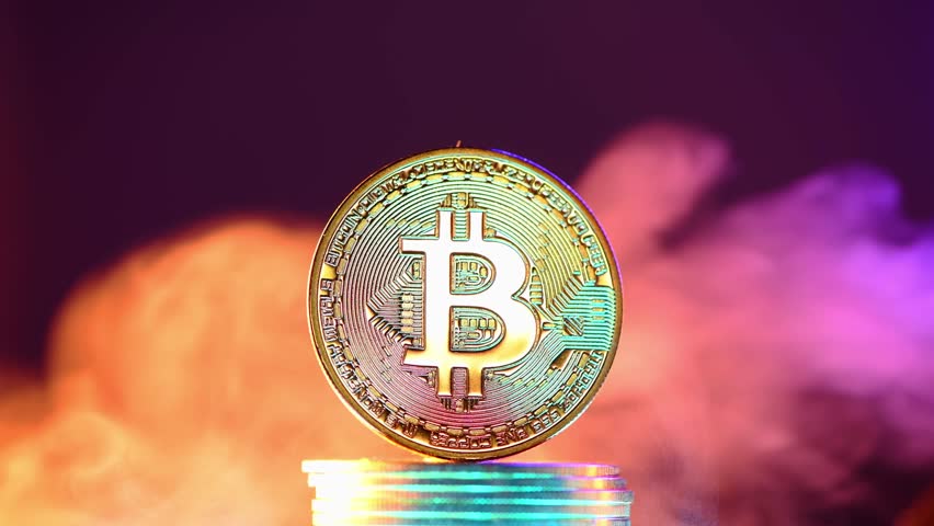 Bitcoin cryptocurrency coin standing on a stack of coins surrounded by colorful smoke on a dark background, representing the volatility and uncertainty of the cryptocurrency market