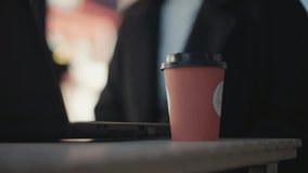 Close-up of laptop on table with hand in black coat, polished nails, dropping a pink coffee cup onto table surface sits down, blurred background - Powered by Shutterstock - Get 15% off with code: PIKWIZARD15