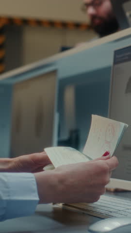 Airport Check-in Counter: Airline Agent Checking Documents, Airplane Ticket in Airport Terminal. Computer Program Analyzing Fingerprint Scanning and Biometric Data for Boarding Flight. Vertical Shot.