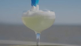 A glass filled with a yellow liquid and a blue straw. The straw is sticking out of the glass, and the liquid is almost overflowing. The glass is placed on a table, and the scene takes place outdoors - Powered by Shutterstock - Get 15% off with code: PIKWIZARD15