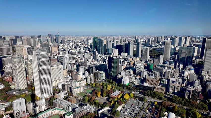 Aerial view of Tokyo cityscape with modern skyscrapers, green parks, and clear blue sky, offering a stunning urban panorama of Minato ward