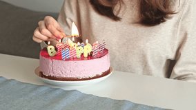 A woman carefully lights letter-shaped birthday candles on a pink mousse cake using a matchstick, preparing for a joyful indoor celebration with warm lighting and a festive atmosphere - Powered by Shutterstock - Get 15% off with code: PIKWIZARD15