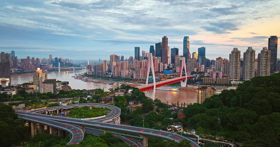 Aerial view of Chongqing cityscape with the bridge and winding roads nestled amongst hills at twilight.
