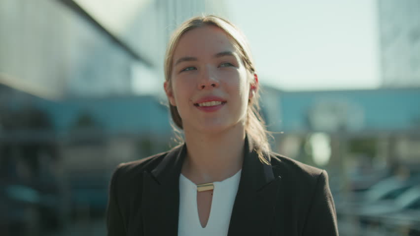 Woman with refreshing look in professional attire walks by modern glass building holding tablet in one hand and takeaway tea in other hand, sipping drink calmly in bright urban outdoor setting