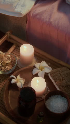 Vertical shot of Caucasian woman lying on massage table with her eyes closed while enjoying relaxing head massage in candlelit spa room