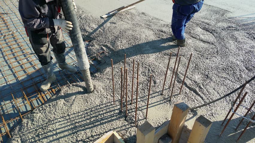 Construction workers with concrete boom pump crane at construction site pouring concrete into a formwork with reinforcement for building a new house