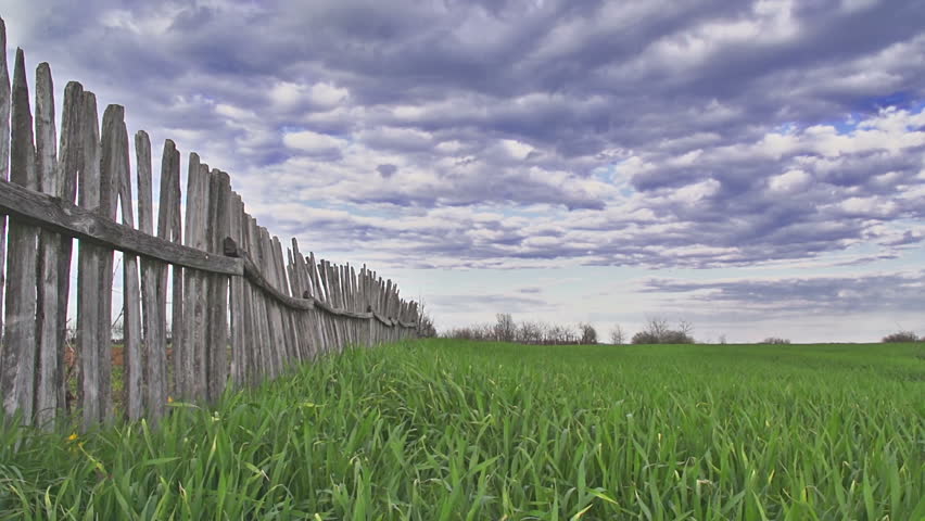 Epic time lapse of storm clouds over green meadow and wooden fence