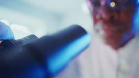 Close up of a scientist wearing safety glasses looking through a microscope, conducting research in a modern laboratory with blue and purple lighting - Powered by Shutterstock - Get 15% off with code: PIKWIZARD15